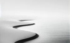 A minimalist black and white beach scene with calm waves gently reaching the shoreline, representing tranquility and relaxation. The empty beach and smooth horizon evoke a peaceful and serene atmosphere, symbolizing stress relief and balance.